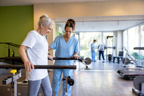 Physical therapist assisting an elderly patient with walking exercises using parallel bars in a rehabilitation gym